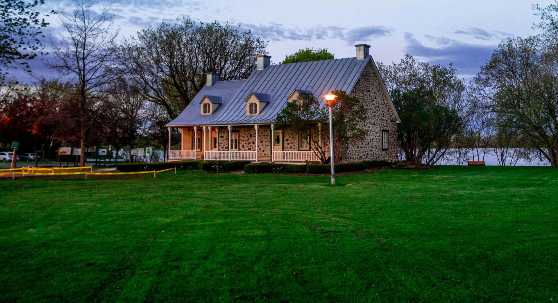 Serene stone house by a lakeside with lush green lawn, ideal for real estate and architectural themes.